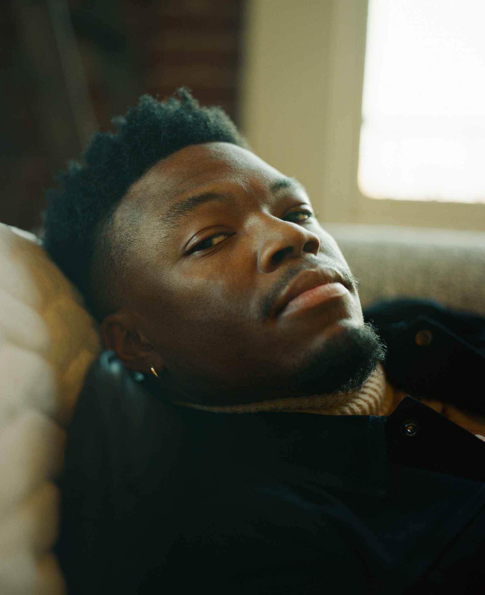 Warm-toned, film-style portrait of Caleb Castille lying on a couch