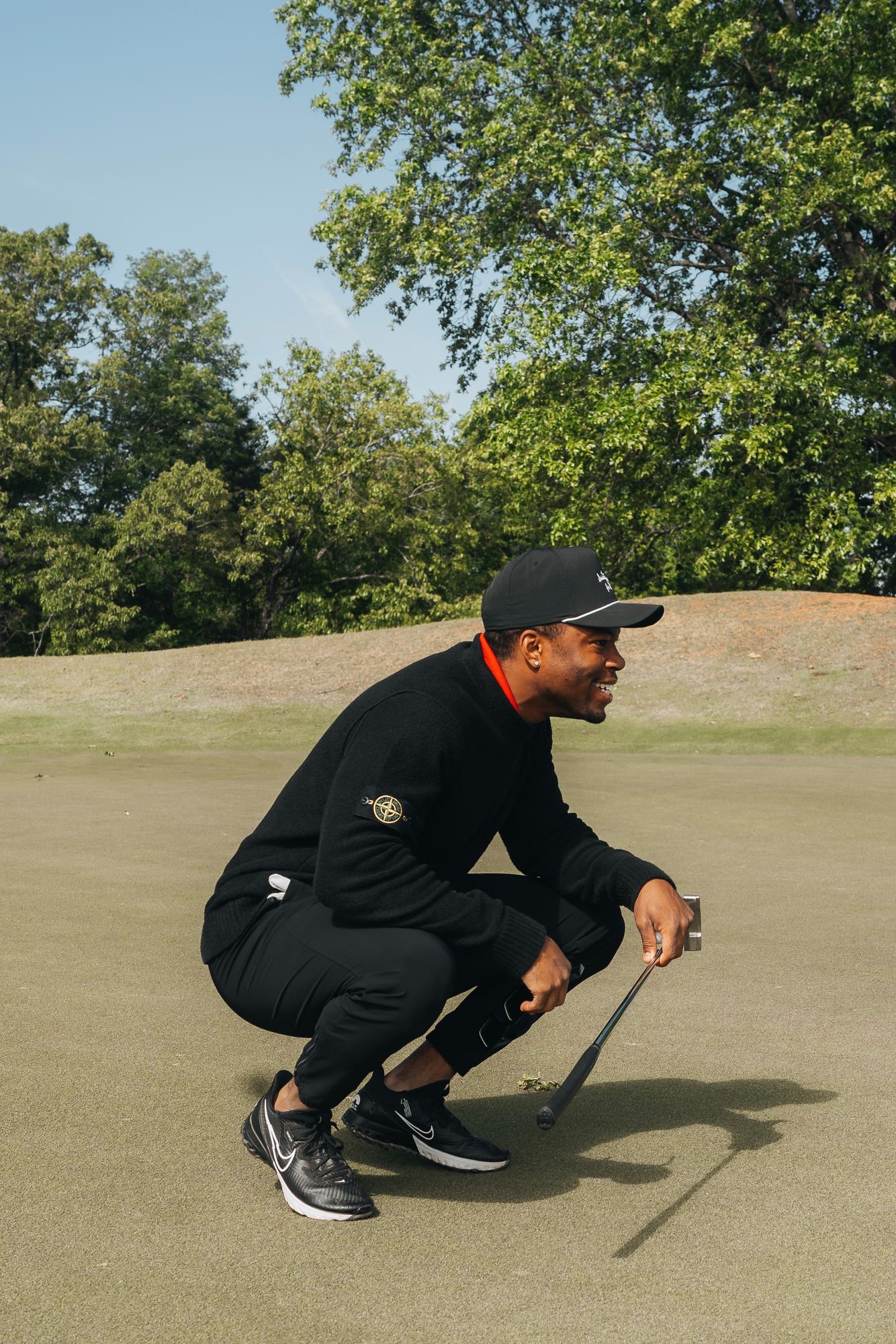 Caleb Castille crouching on a golf course in a black outfit and cap