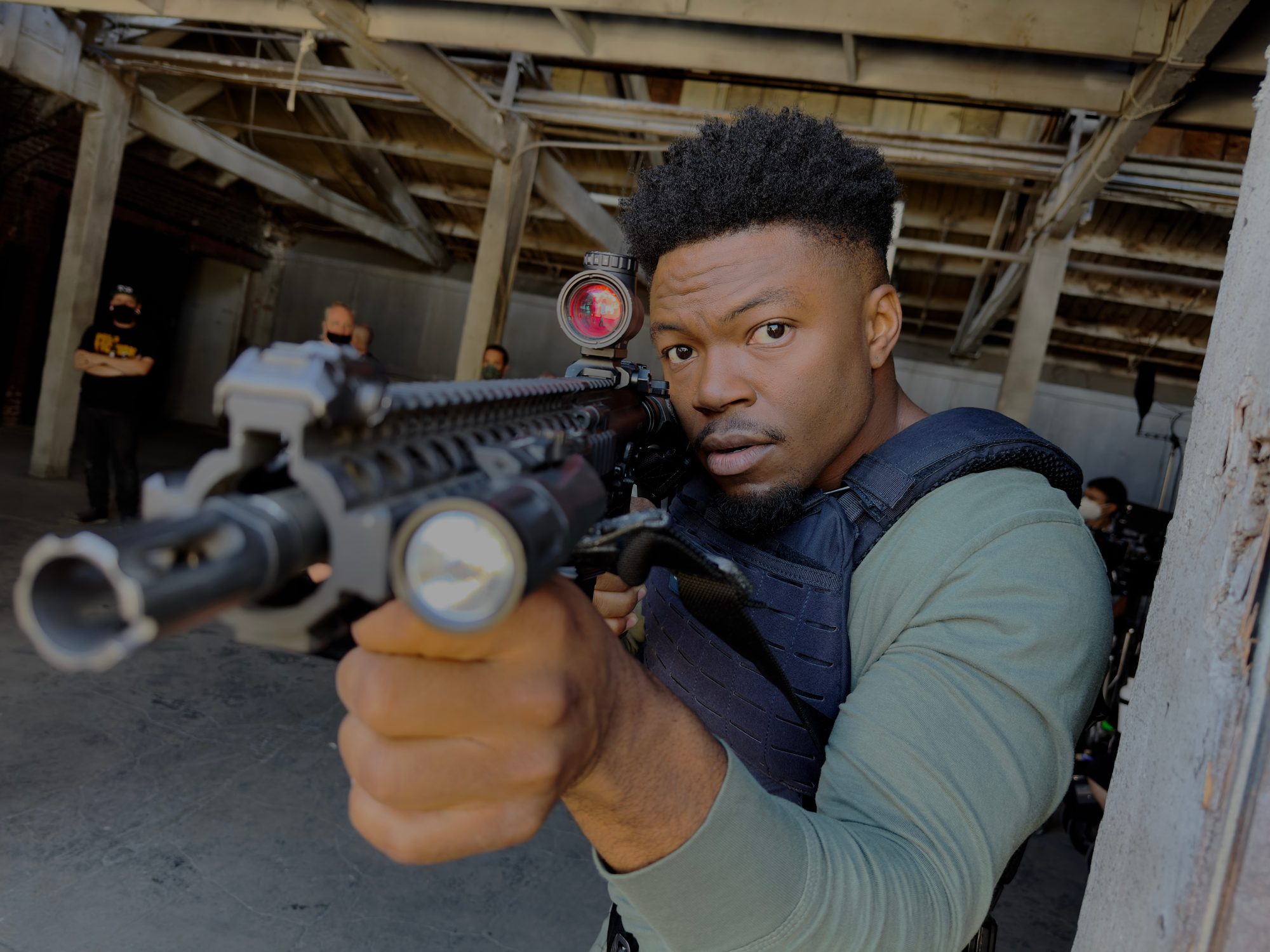 Caleb Castille in a tactical vest pointing a rifle toward the camera