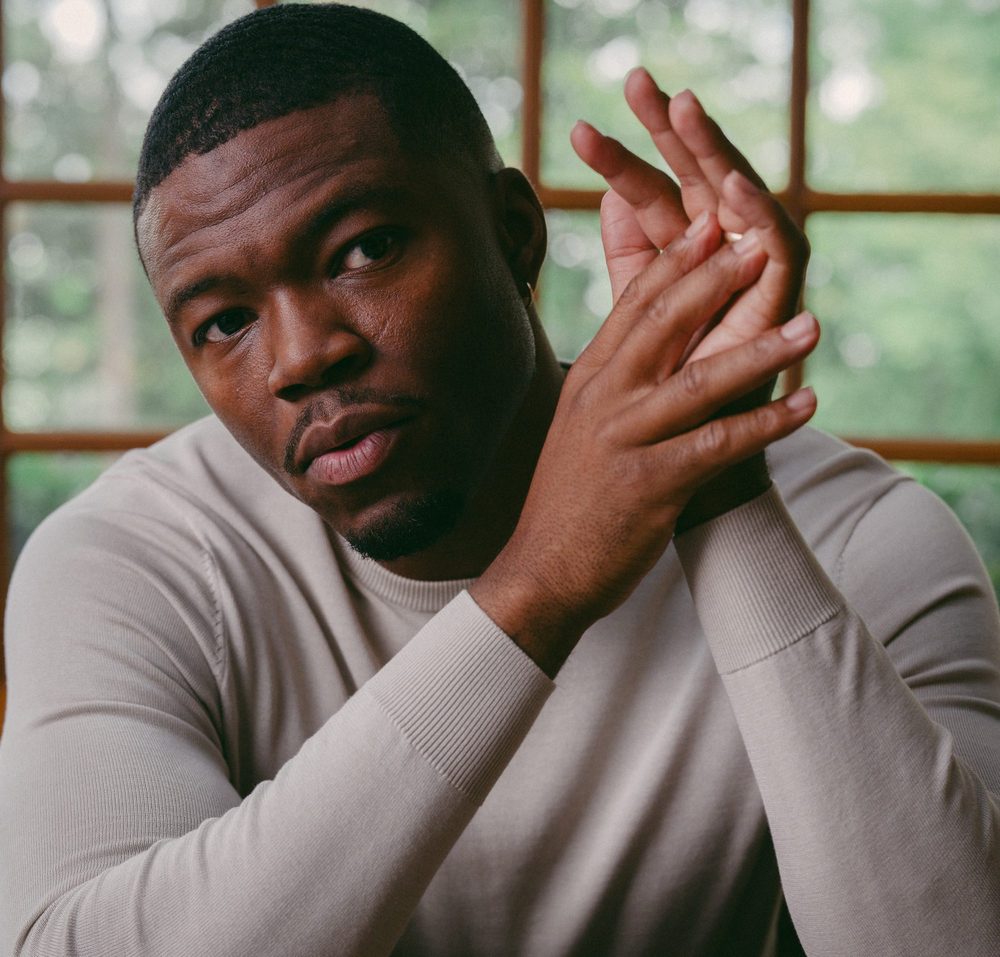 Caleb Castille in a beige sweater, hands pressed together, looking into the camera