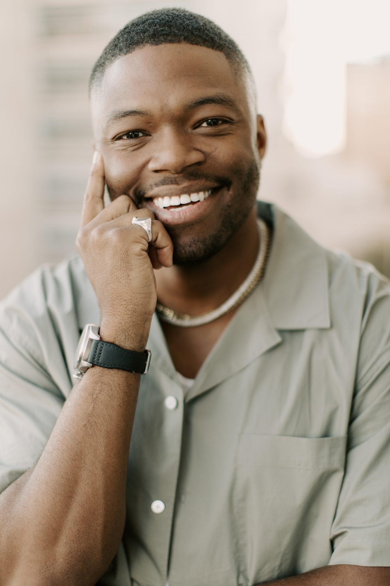 Caleb Castille smiling in an olive shirt with one hand at his face