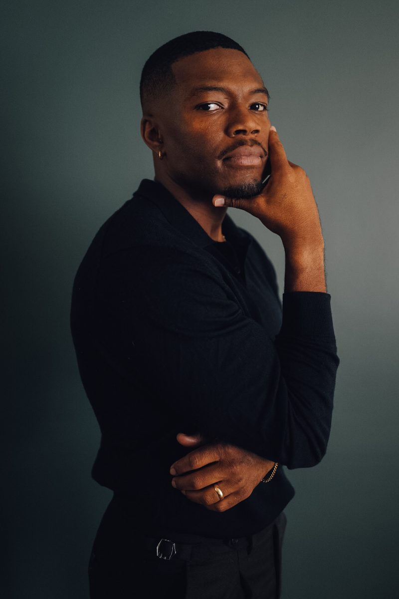Caleb Castille in a dark studio portrait with his hand at his chin